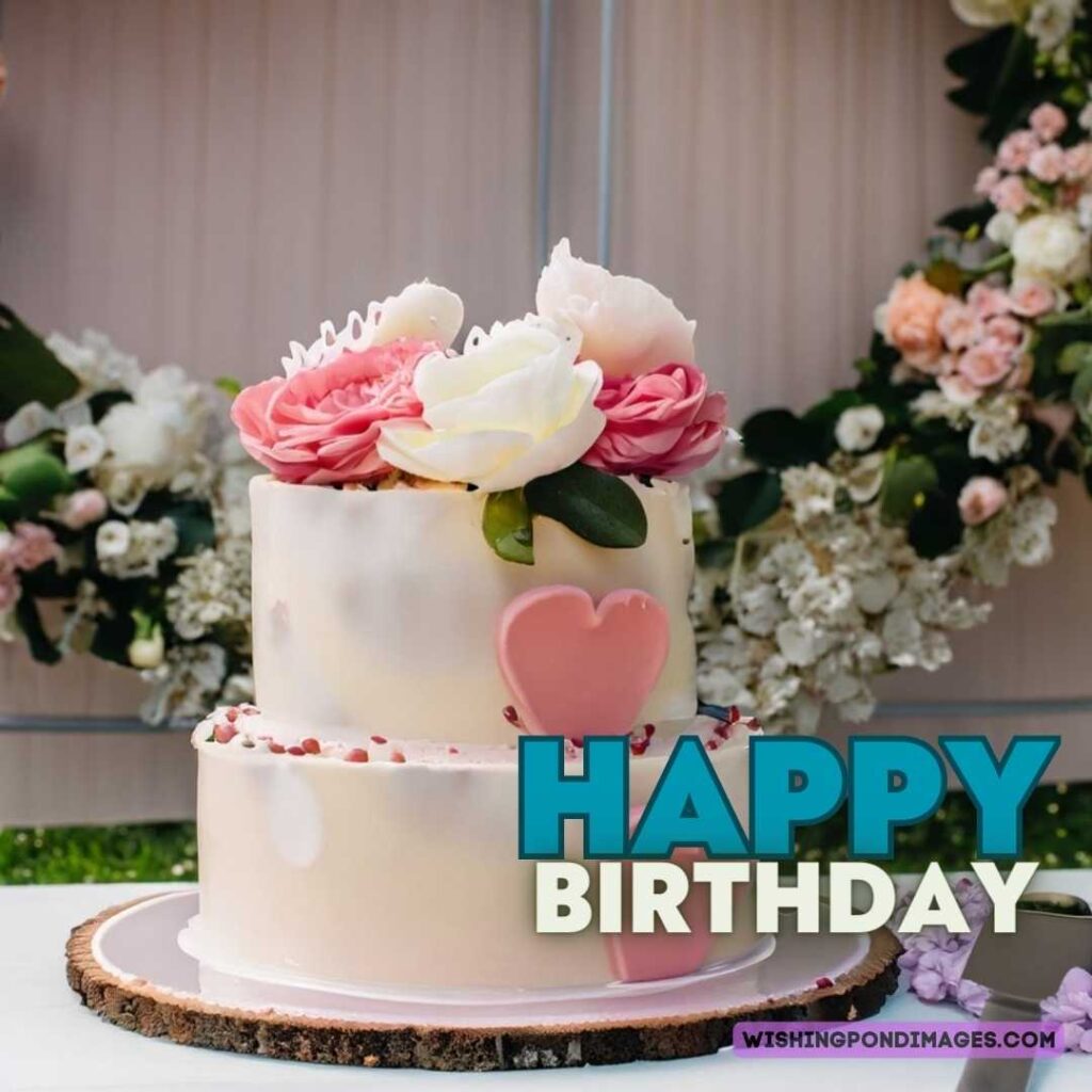 Layered birthday cake with flower decoration on top of flowers on the wall background. Happy birthday cake flowers images